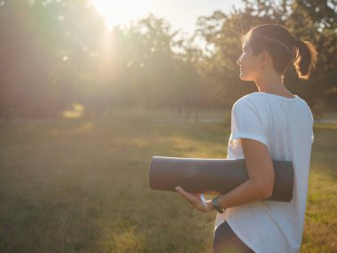 Şehir parkında sağlıklı aktif yaşam tarzı kavramı. Kadın yaz günü spor paspasıyla parkta yürürken, sağlık durumu, sağlık egzersizi ya da açık hava egzersizinden sonra ya da öncesinde.
