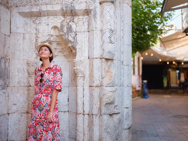 Antalya, Türkiye 'ye yaz seyahati. Kırmızı elbiseli genç Asyalı kadın eski şehir Kalechi 'den geçiyor. Kadın turist ilginç yerler ve popüler turistik ilgi alanları keşfediyor.