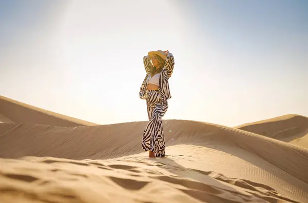 Desert adventure. Young arabian Woman in zebra suits and hat in sands dunes of UAE desert at sunset. The Dubai Desert Conservation Reserve, United Arab Emirates.