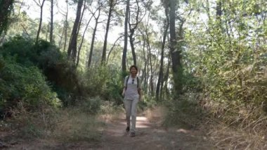 Yürüyüş. Sırt çantalı ve şapkalı bir kadın Türkiye 'de deniz kenarındaki çam ormanlarında yürüyor. Ormanda yürüyüş. Orman yürüyüşünde altın ışık. Güneşli bir yaz günü. Ağaçların arasında yürüyorum. Tatil tatili doğanın tadını çıkarıyor.