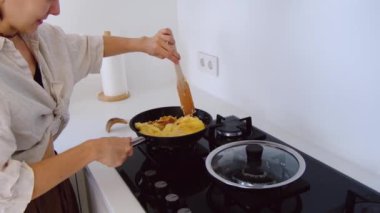 Mutfaktaki kadın ev ödevi yapıyor. Kadın omleti peynirle karıştırıyor ve tavada fırında kızartıyor. İç mekan mutfağı. Kahvaltı hazırlığı..