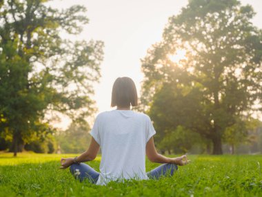 Genç Asyalı bir kadın sabah veya akşam parkta meditasyon yapıyor sağlıklı bir kadın şehir parkında yoga yapıyor. Farkındalık, kararlılık, sağlıklı alışkanlıklar ve denge konsepti