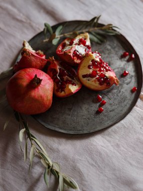 Eski bir retro plaka üzerinde Türk Narı ve zeytin dalı ile Still Life 'ın görüntüsü. Karanlık ahşap arka plan, antika bakır plaka. Taze taze nar, açık nar ve tohum.