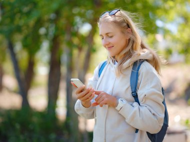 Şehir parkında akıllı telefon kullanan genç ve güzel bir kadın. Dışarıda cep telefonuyla mesajlaşan gülümseyen kız öğrenci. Modern yaşam tarzı, bağlantı, gelişigüzel iş kavramı