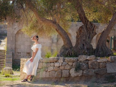 Beyaz elbiseli güzel Asyalı genç kadın. Rodos Akropolü. Stadyum ve tiyatro gibi çeşitli binalarla antik yerleşim yerlerinin ünlü kalıntıları..