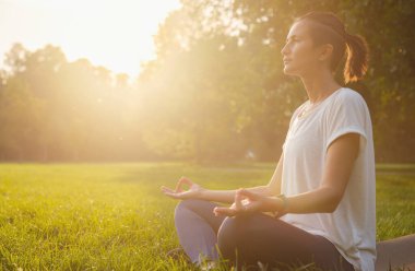 Genç Asyalı bir kadın sabah veya akşam parkta meditasyon yapıyor sağlıklı bir kadın şehir parkında yoga yapıyor. Farkındalık, kararlılık, sağlıklı alışkanlıklar ve denge konsepti