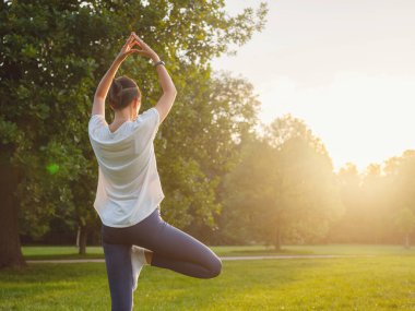 Genç Asyalı bir kadın sabah ya da akşam parkta yoga yapıyor sağlıklı bir kadın şehir parkında ağaç pozu veriyor. Farkındalık, kararlılık, sağlıklı alışkanlıklar ve denge konsepti