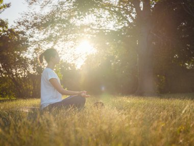 Genç Asyalı bir kadın sabah veya akşam parkta meditasyon yapıyor sağlıklı bir kadın şehir parkında yoga yapıyor. Farkındalık, kararlılık, sağlıklı alışkanlıklar ve denge konsepti