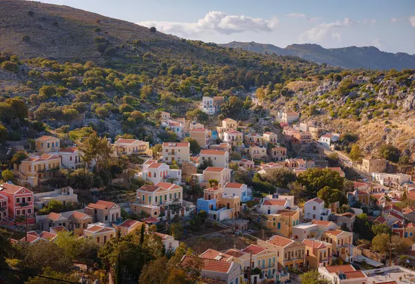 Symi Adası, Yunanistan. Yunanistan, Ege Denizi 'ndeki Rodos adalarından tatil yapıyor. Günbatımında bir Yunan adasının yamaçlarında renkli neoklasik güzel evler. Tatil seyahat arkaplanı.