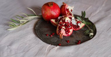 Eski bir retro plaka üzerinde Türk Narı ve zeytin dalı ile Still Life 'ın görüntüsü. Karanlık ahşap arka plan, antika bakır plaka. Taze taze nar, açık nar ve tohum.