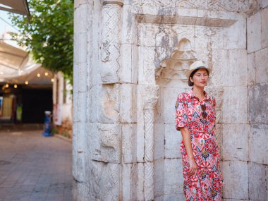 Antalya, Türkiye 'ye yaz seyahati. Kırmızı elbiseli genç Asyalı kadın eski şehir Kalechi 'den geçiyor. Kadın turist ilginç yerler ve popüler turistik ilgi alanları keşfediyor.