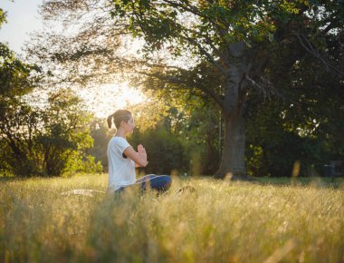 Genç Asyalı bir kadın sabah veya akşam parkta meditasyon yapıyor sağlıklı bir kadın şehir parkında yoga yapıyor. Farkındalık, kararlılık, sağlıklı alışkanlıklar ve denge konsepti