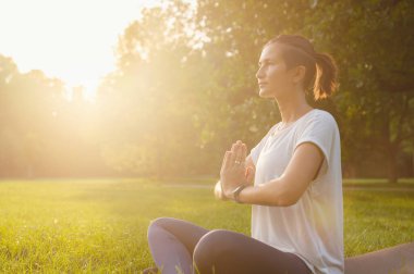 Genç Asyalı bir kadın sabah veya akşam parkta meditasyon yapıyor sağlıklı bir kadın şehir parkında yoga yapıyor. Farkındalık, kararlılık, sağlıklı alışkanlıklar ve denge konsepti