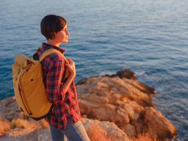 İspanya, Benidorm 'da kayalık sahilde yürüyüş yapan genç bir kadın. Dalgalı denizi ve körfezi izliyorum. Gezgin, huzurlu doğa manzarasında özgürlüğün tadını çıkarıyor.
