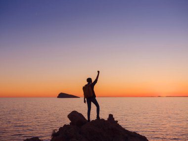 İspanya, Benidorm 'da kayalık plajda yürüyüş yapan genç bir kadının silueti. Dalgalı denizi ve körfezi izliyorum. Huzurlu günbatımı manzarasında özgürlüğün tadını çıkaran gezgin, başarı konsepti