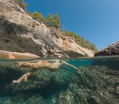 Bayramlarda genç bir kadın, Antalya Türkiye 'nin kristal berrak su sahilinde yüzmenin keyfini çıkarıyor. Kolları açık yüzen Asyalı güzel bir kadın. Rahatla ve sakinleş. Seyahat ve Tatil kavramı.