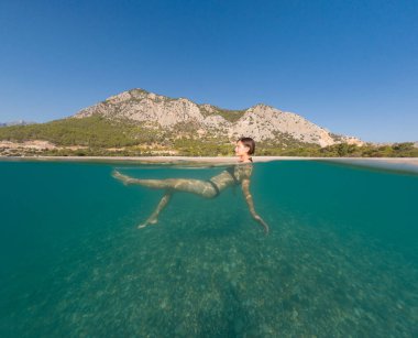 Bayramlarda genç bir kadın, Antalya Türkiye 'nin kristal berrak su sahilinde yüzmenin keyfini çıkarıyor. Kolları açık yüzen Asyalı güzel bir kadın. Rahatla ve sakinleş. Seyahat ve Tatil kavramı.