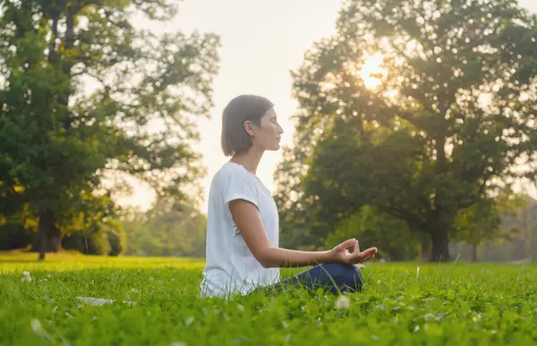 Genç Asyalı bir kadın sabah veya akşam parkta meditasyon yapıyor sağlıklı bir kadın şehir parkında yoga yapıyor. Farkındalık, kararlılık, sağlıklı alışkanlıklar ve denge konsepti