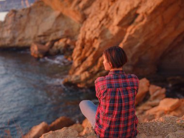 İspanya, Benidorm 'da kayalık sahilde yürüyüş yapan genç bir kadın. Dalgalı denizi ve körfezi izliyorum. Gezgin, huzurlu doğa manzarasında özgürlüğün tadını çıkarıyor.