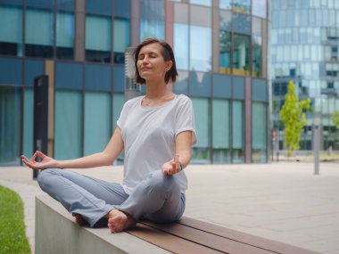 Stres atma, rahatlama fikri. Ofiste geçirdiği yoğun bir günün ardından cam gökdelenlerin altında el ele tutuşarak yoga egzersizleri yapan barışçıl kadın serbest çalışan.