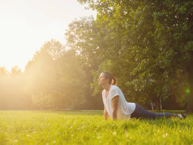 Genç Asyalı bir kadın sabah ya da akşam parkta yoga yapıyor sağlıklı bir kadın şehir parkında Upward Facing Dog Poose 'da dinleniyor. Farkındalık, kararlılık, sağlıklı alışkanlıklar ve denge konsepti