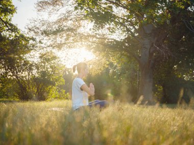 Genç Asyalı bir kadın sabah veya akşam parkta meditasyon yapıyor sağlıklı bir kadın şehir parkında yoga yapıyor. Farkındalık, kararlılık, sağlıklı alışkanlıklar ve denge konsepti