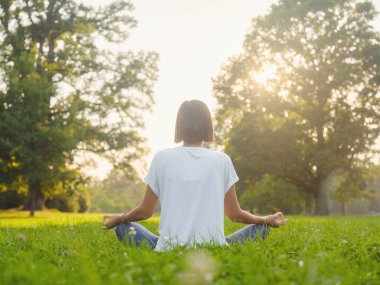 Genç Asyalı bir kadın sabah veya akşam parkta meditasyon yapıyor sağlıklı bir kadın şehir parkında yoga yapıyor. Farkındalık, kararlılık, sağlıklı alışkanlıklar ve denge konsepti