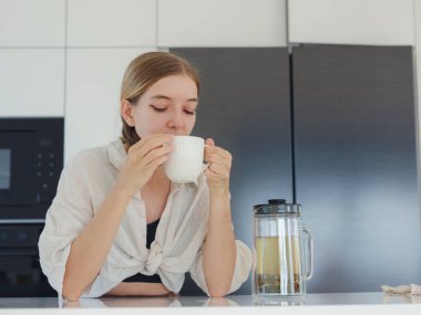 Bitki çayı, çay fincanı ve kahve makinası yapmak, beyaz modern mutfakta ev işi yapmak. Mutfakta çay içmek ve dinlenmek, güne olumlu düşüncelerle başlamak için.