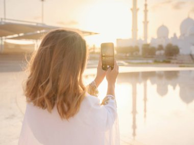 Abu Dabi 'deki Birleşik Arap Emirlikleri' ne git. Beyaz Arap elbiseli kadın, Şeyh Zayed Büyük Beyaz Camii 'nin telefonuyla resim yapıyor. Ünlü Abu Dabi gezisi..