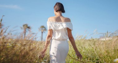 Çiçek tarlasında beyaz elbiseli güzel bir Asyalı genç kadın. Temiz havayı kucaklamak ve açık hava aktivitelerine katılmak. Friluftsliv konsepti, dışarıda mümkün olduğunca çok zaman geçirmek demektir.