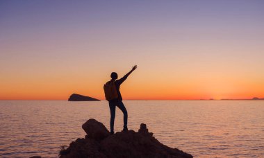 İspanya, Benidorm 'da kayalık plajda yürüyüş yapan genç bir kadının silueti. Dalgalı denizi ve körfezi izliyorum. Huzurlu günbatımı manzarasında özgürlüğün tadını çıkaran gezgin, başarı konsepti