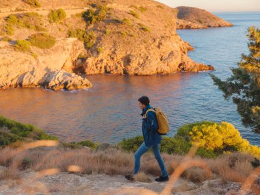 İspanya, Benidorm 'da kayalık sahilde yürüyüş yapan genç bir kadın. Dalgalı denizi ve körfezi izliyorum. Gezgin, huzurlu doğa manzarasında özgürlüğün tadını çıkarıyor.