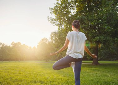 Genç Asyalı bir kadın sabah ya da akşam parkta yoga yapıyor sağlıklı bir kadın şehir parkında ağaç pozu veriyor. Farkındalık, kararlılık, sağlıklı alışkanlıklar ve denge konsepti