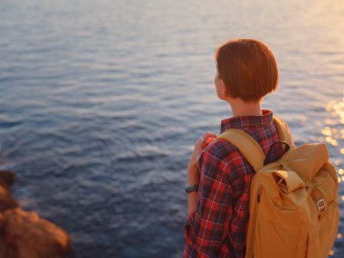 İspanya, Benidorm 'da kayalık sahilde yürüyüş yapan genç bir kadın. Dalgalı denizi ve körfezi izliyorum. Gezgin, huzurlu doğa manzarasında özgürlüğün tadını çıkarıyor.