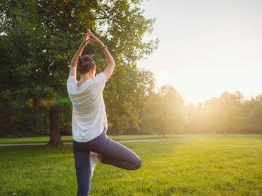 Genç Asyalı bir kadın sabah ya da akşam parkta yoga yapıyor sağlıklı bir kadın şehir parkında ağaç pozu veriyor. Farkındalık, kararlılık, sağlıklı alışkanlıklar ve denge konsepti