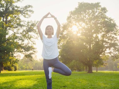 Genç Asyalı bir kadın sabah ya da akşam parkta yoga yapıyor sağlıklı bir kadın şehir parkında ağaç pozu veriyor. Farkındalık, kararlılık, sağlıklı alışkanlıklar ve denge konsepti