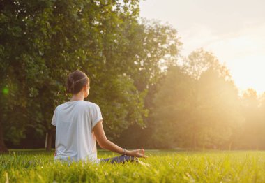 Genç Asyalı bir kadın sabah veya akşam parkta meditasyon yapıyor sağlıklı bir kadın şehir parkında yoga yapıyor. Farkındalık, kararlılık, sağlıklı alışkanlıklar ve denge konsepti