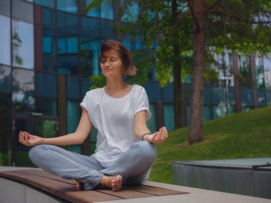 Stres atma, rahatlama fikri. Ofiste geçirdiği yoğun bir günün ardından cam gökdelenlerin altında el ele tutuşarak yoga egzersizleri yapan barışçıl kadın serbest çalışan.