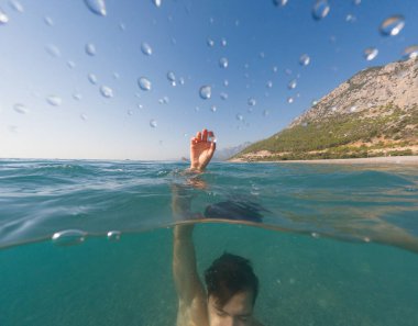 Deniz yazı manzarası. Genç adam, suyun altında ve üstünde, denize batıyor.,