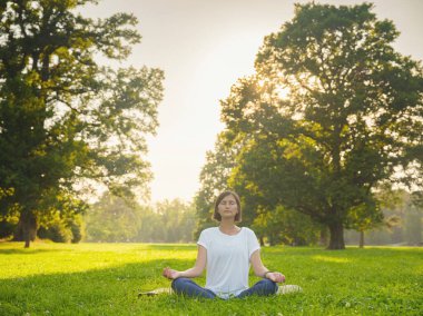 Genç Asyalı bir kadın sabah veya akşam parkta meditasyon yapıyor sağlıklı bir kadın şehir parkında yoga yapıyor. Farkındalık, kararlılık, sağlıklı alışkanlıklar ve denge konsepti