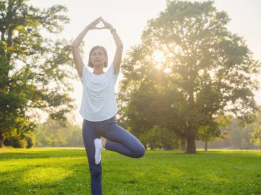Genç Asyalı bir kadın sabah ya da akşam parkta yoga yapıyor sağlıklı bir kadın şehir parkında ağaç pozu veriyor. Farkındalık, kararlılık, sağlıklı alışkanlıklar ve denge konsepti