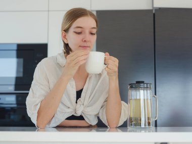 Bitki çayı, çay fincanı ve kahve makinası yapmak, beyaz modern mutfakta ev işi yapmak. Mutfakta çay içmek ve dinlenmek, güne olumlu düşüncelerle başlamak için.