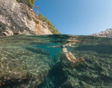 Bayramlarda genç bir kadın, Antalya Türkiye 'nin kristal berrak su sahilinde yüzmenin keyfini çıkarıyor. Kolları açık yüzen Asyalı güzel bir kadın. Rahatla ve sakinleş. Seyahat ve Tatil kavramı.
