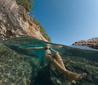 Bayramlarda genç bir kadın, Antalya Türkiye 'nin kristal berrak su sahilinde yüzmenin keyfini çıkarıyor. Kolları açık yüzen Asyalı güzel bir kadın. Rahatla ve sakinleş. Seyahat ve Tatil kavramı.
