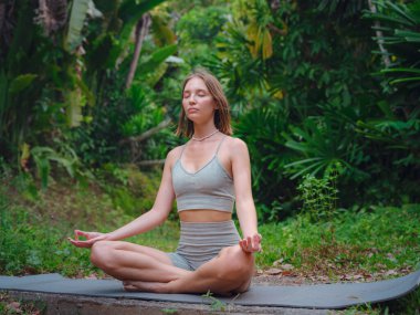 Güzel bir kadın sabahları Tayland, Crabi 'de havuz başında yoga yapıyor. Lotus 'ta oturan neşeli kadın portresi ormanda yoga sırasında zihinsel ve fiziksel gücünü koruyor.