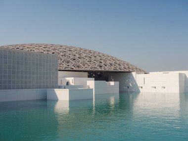 Abu Dabi, Birleşik Arap Emirlikleri - 13 Ocak 2024: Louvre Abu Dabi ünlü müzesinin dışı. Zümrüt yeşili hendeği çevreleyen düz beyaz duvarlar süslü bir kubbe çatısı ile kaplı.