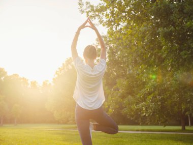 Genç Asyalı bir kadın sabah ya da akşam parkta yoga yapıyor sağlıklı bir kadın şehir parkında ağaç pozu veriyor. Farkındalık, kararlılık, sağlıklı alışkanlıklar ve denge konsepti