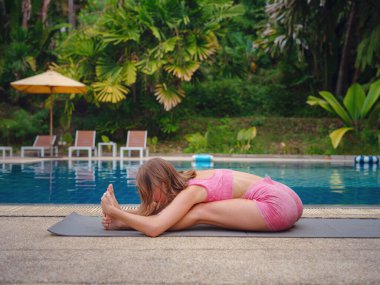 Kadın vücut egzersizi yapıyor zayıf ve sportif kadınlara ilham veriyor. Sabah doğada havuz başında yeşillik eşliğinde yoga antrenmanından zevk alıyor.