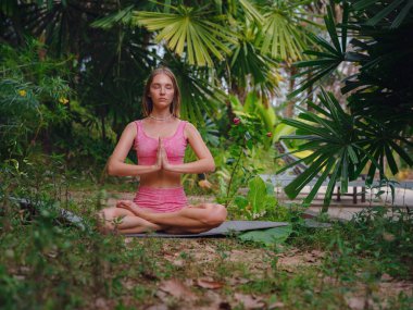 Güzel bir kadın sabahları Tayland, Crabi 'de havuz başında yoga yapıyor. Lotus 'ta oturan neşeli kadın portresi ormanda yoga sırasında zihinsel ve fiziksel gücünü koruyor.