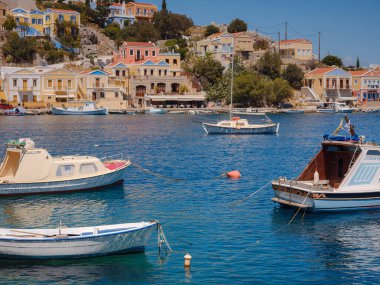 Suriye Adası, Yunanistan - 20 Nisan 2023: Suriye Adası, sakin atmosferli ziyaretçileri hayrete düşüren küçük bir Dodecanese adasıdır. Rengârenk Yunan evlerinin arka planında ada koyunda küçük balıkçı tekneleri
